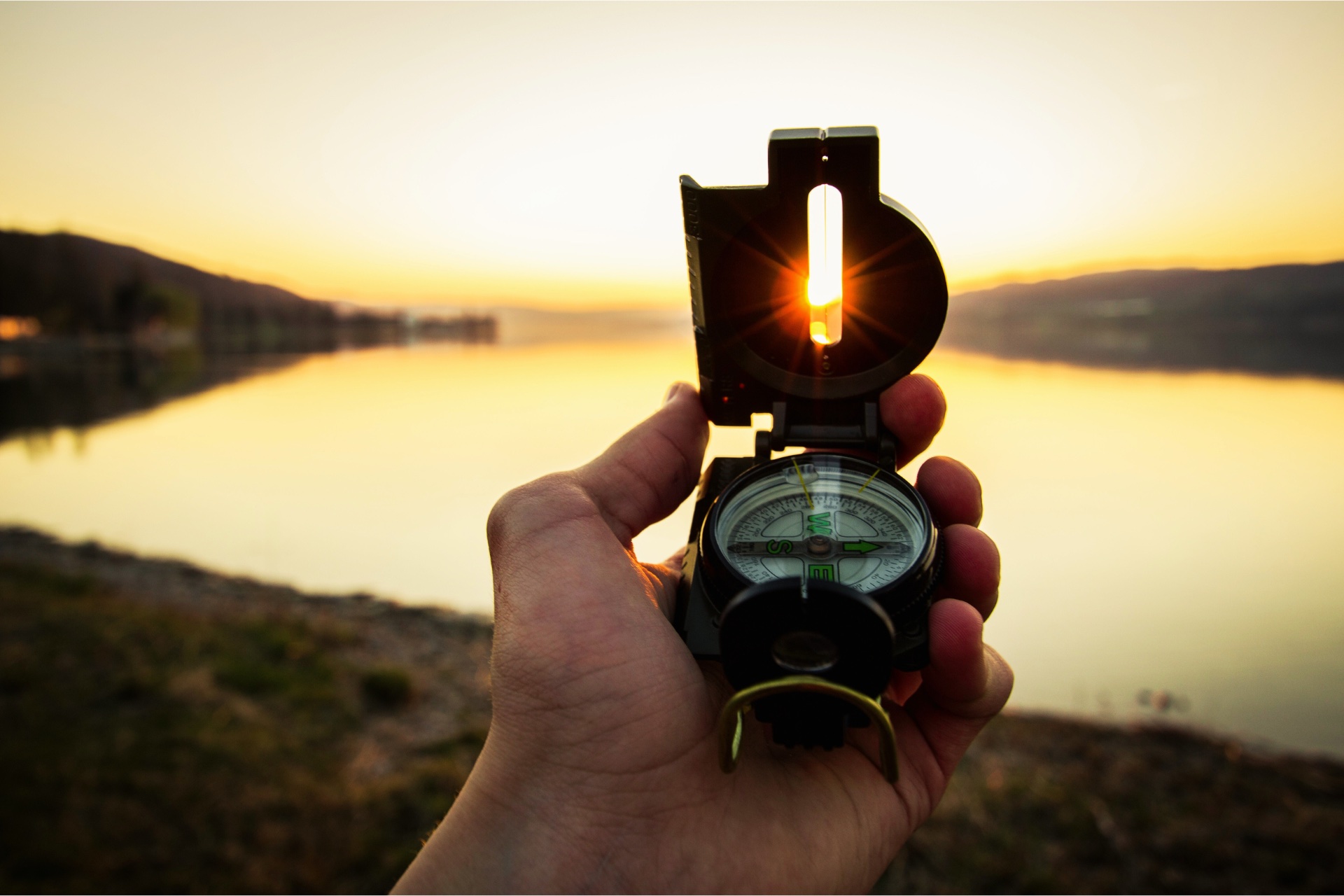 Main tenant une boussole au coucher du soleil symbolisant l’orientation professionnelle